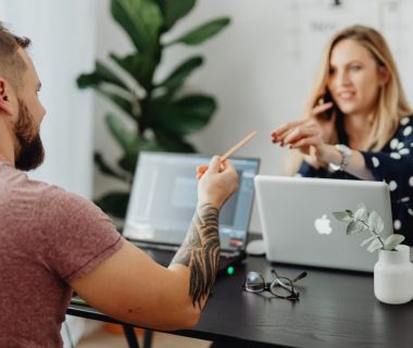 Man and woman discussing work at a table with laptops in a modern office.
