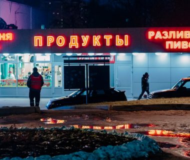 man in black jacket and black pants standing near red and white UNKs store during