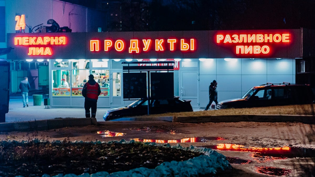 man in black jacket and black pants standing near red and white UNKs store during